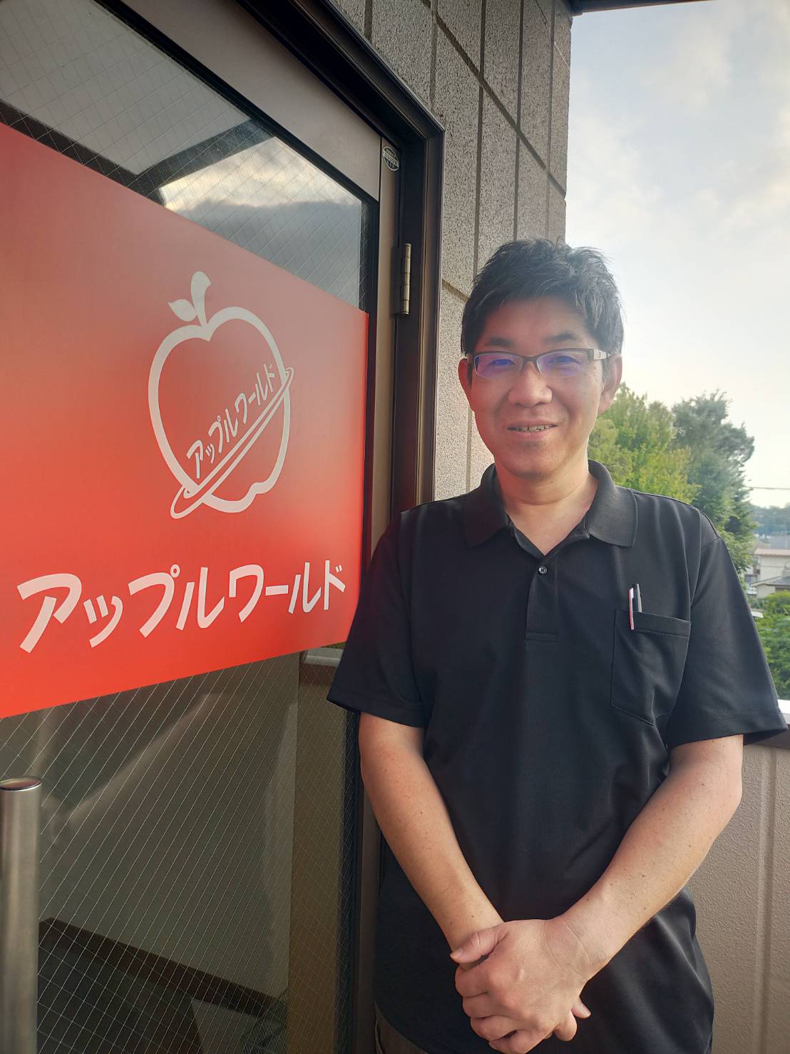 アップルワールド羽村店の看板前に立つ店長 滝内