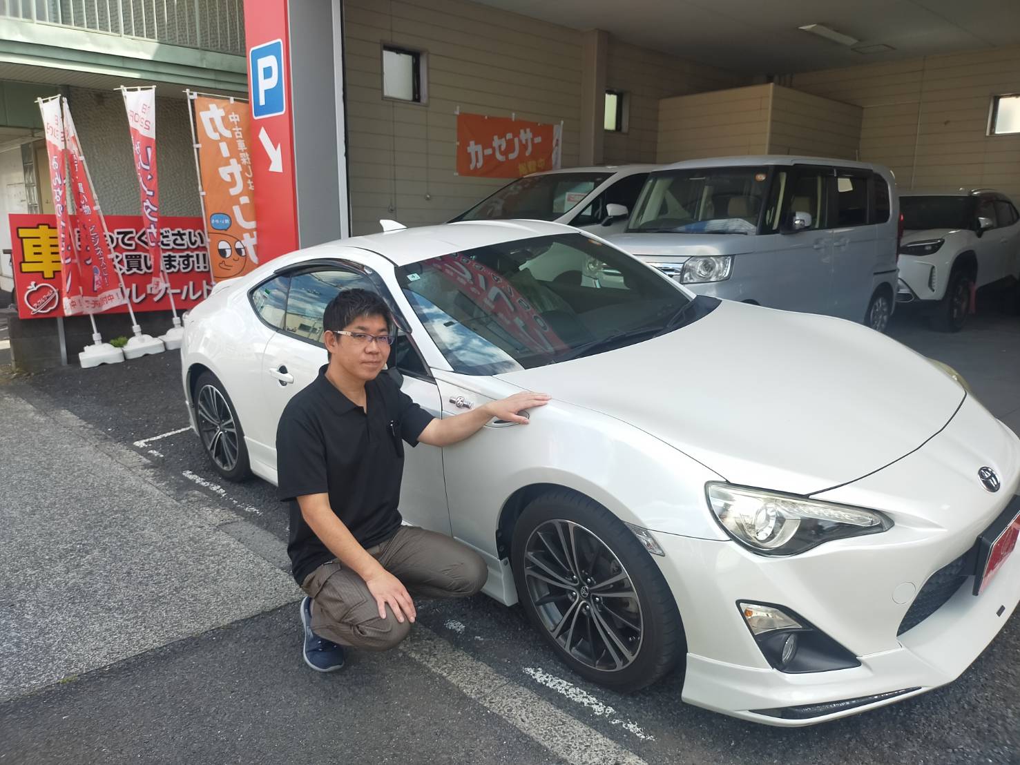 車に手を添えるアップルワールド羽村店 店長 滝内